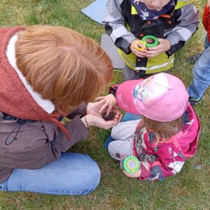 Mithilfe Bildungsarbeit Eine erwachsene Person hockt mit zwei Kinder auf der Wiese. Sie hält eine Kröte in der Hand. Die Kinder schauen und streicheln die Kröte