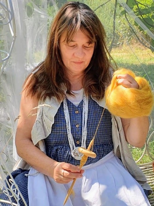 Petra Voß Petra Voß sitzt und spinnt gelbe Wolle mit einer Handspindel