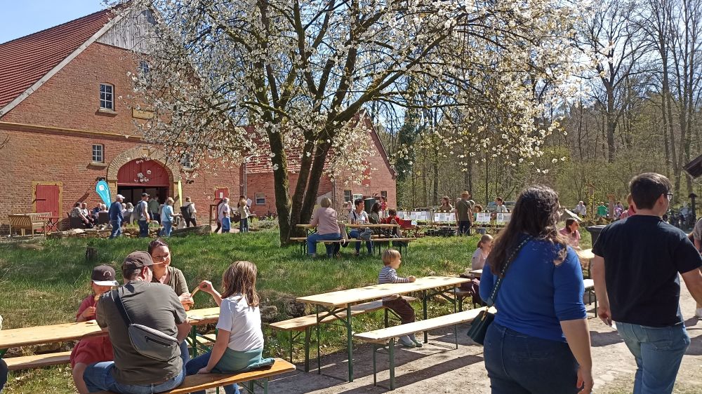 Blick vor der Scheune Richtung Haupthaus, viele Besucher laufen herum, auf Bierzeltgarnituren sitzen Menschen und machen Pause