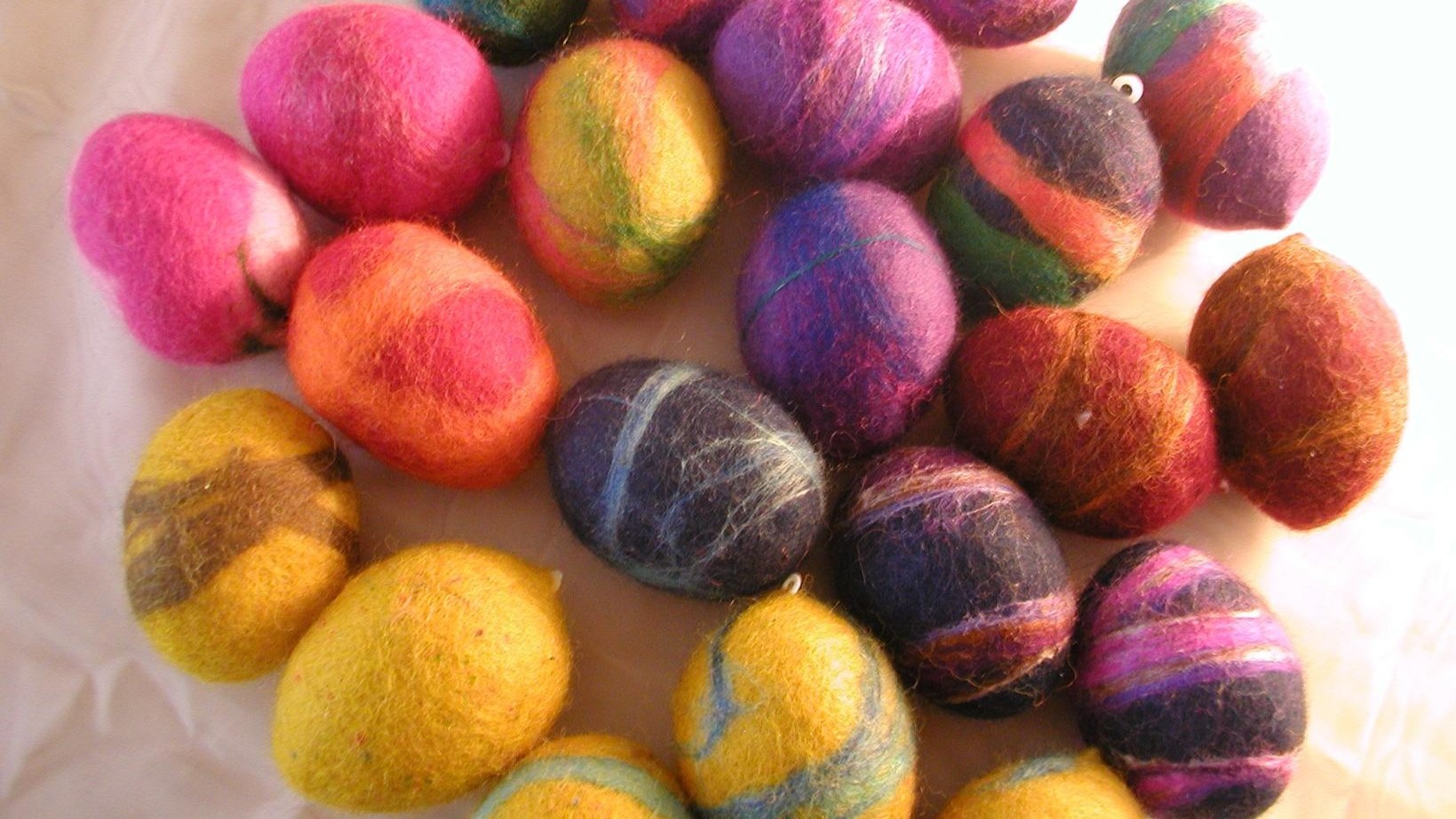 bunt marmorierte, gefilzte Ostereier liegen auf einem hellen Tuch