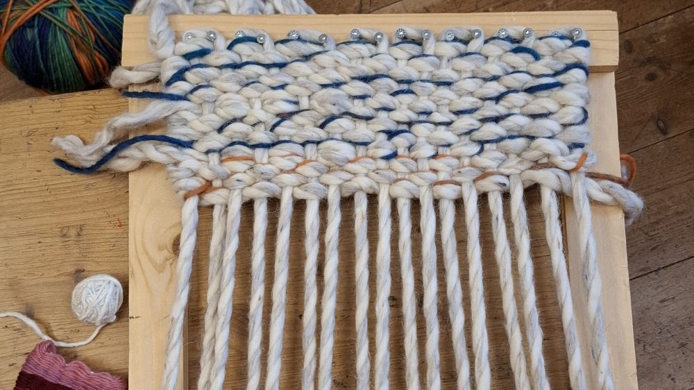 Holzwebrahmen mit dicken Wollfäden bewebt