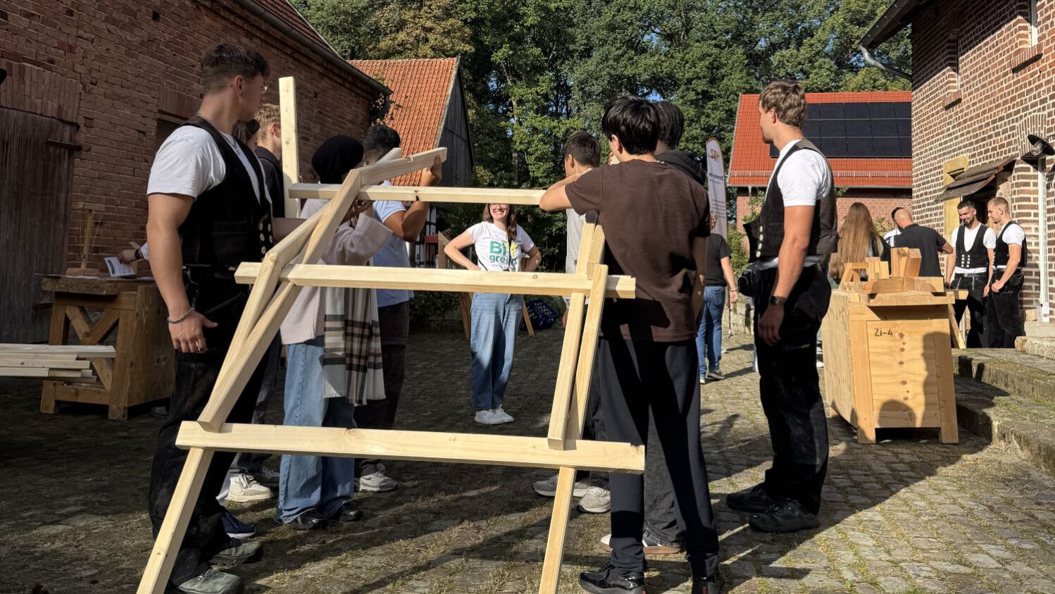 Einblick Zimmerei Mehrere Jugendliche bauen unter Antleitung von Zimmerern einen selbsttragenden Holzbogen aus einfachen Kanthölzern